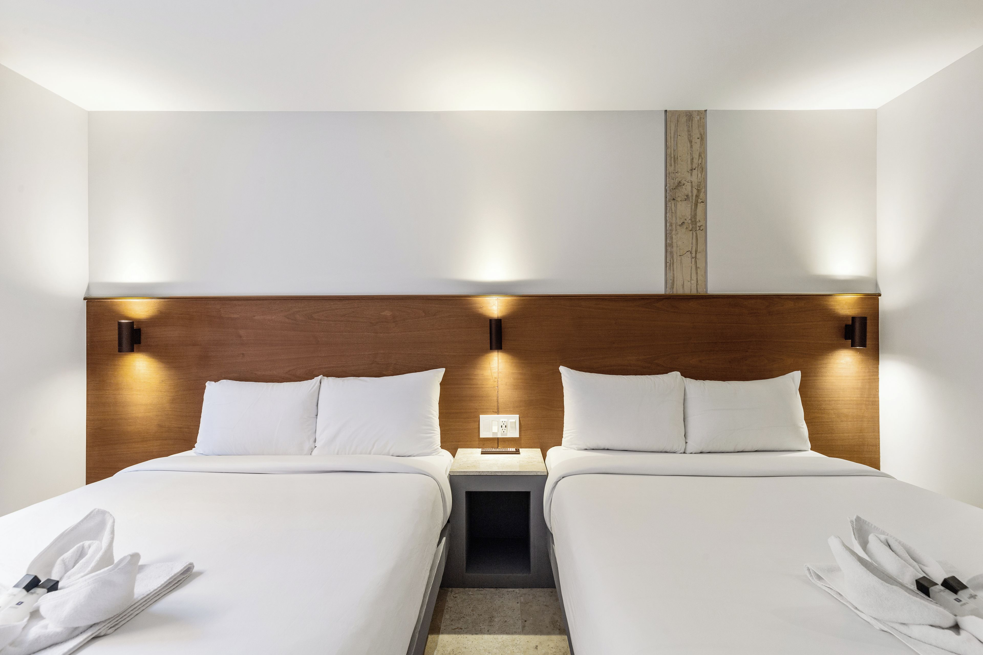 A hotel room with two beds, a wooden headboard, bedside tables, and a nightstand with a remote control.
