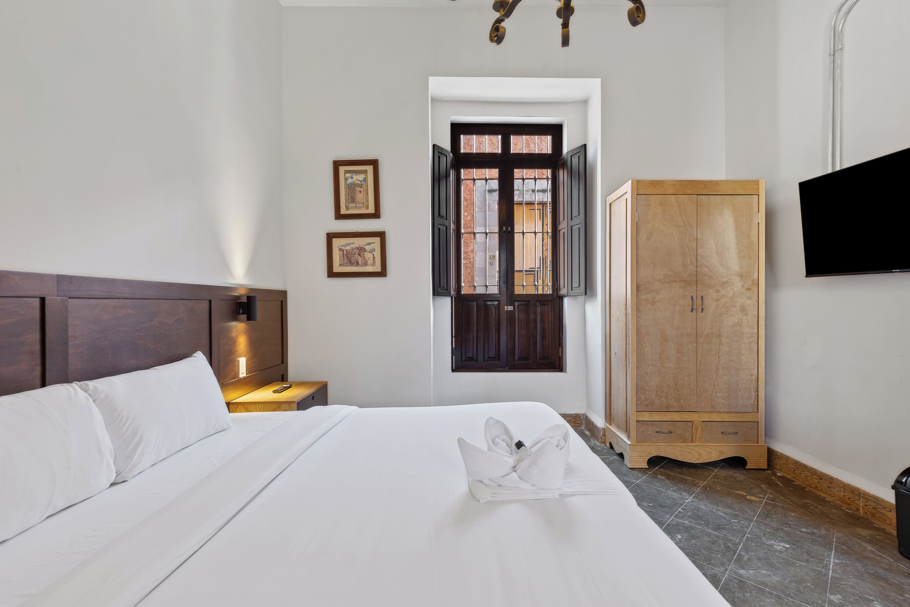 A hotel room with a bed, a nightstand, a wardrobe, a television, and a door with a window.