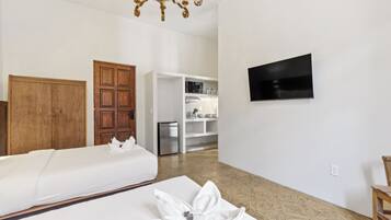 A hotel room with two beds, a wooden wardrobe, a kitchenette, and a flat-screen TV.
