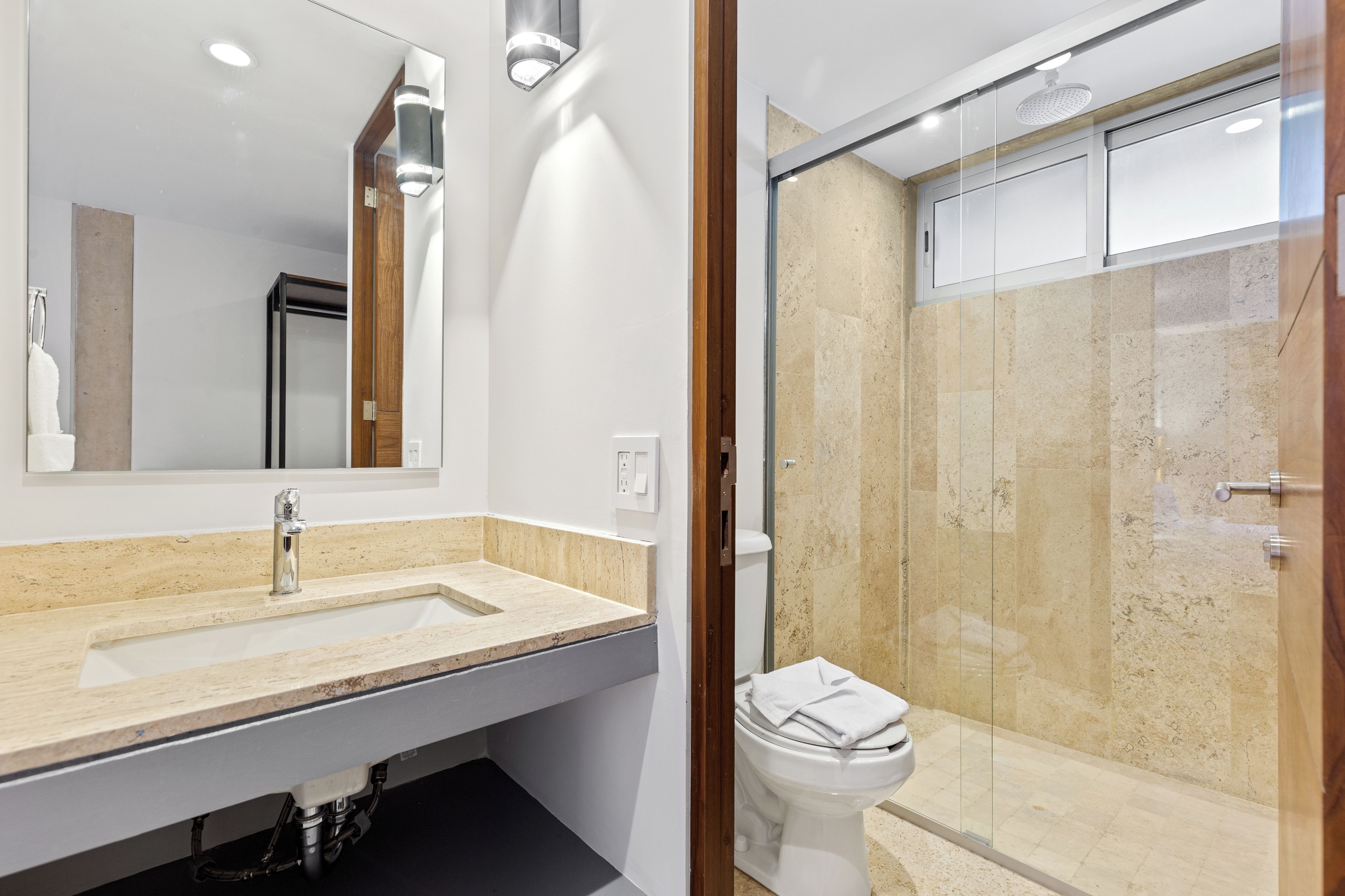 Une salle de bain moderne avec un grand miroir, un lavabo, des toilettes et une douche à parois de verre.