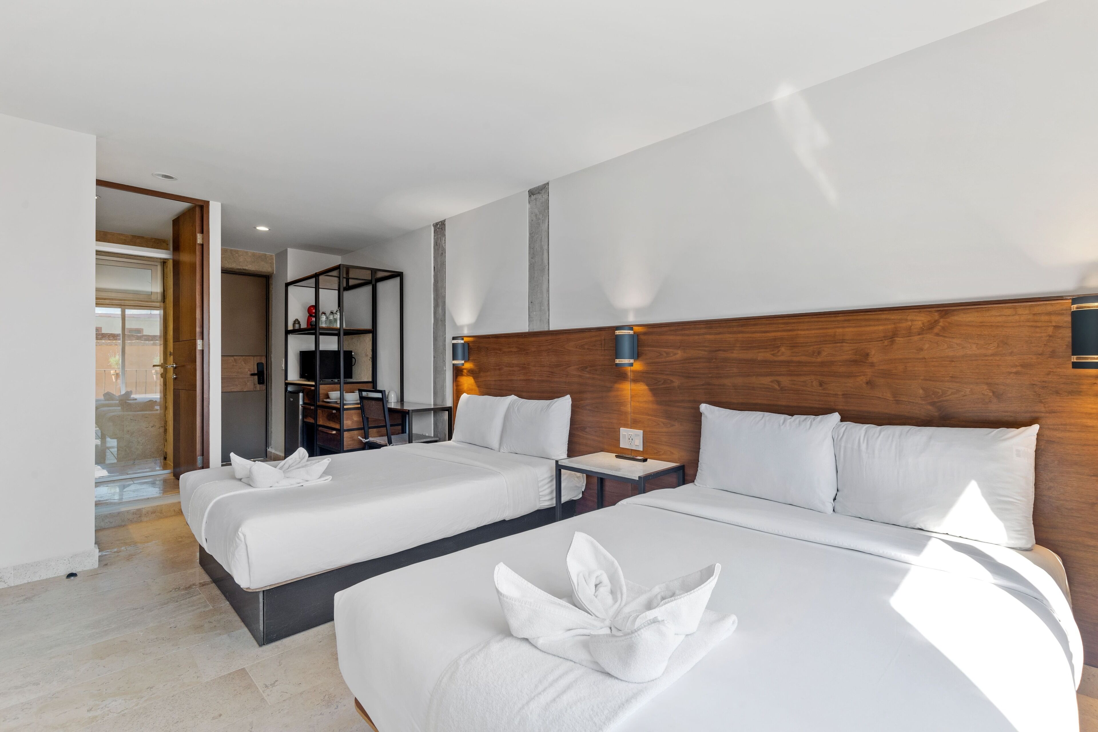 Ein Hotelzimmer mit zwei Betten, einem Holz-Kopfteil, einem kleinen Schreibtisch und Blick ins Freie.