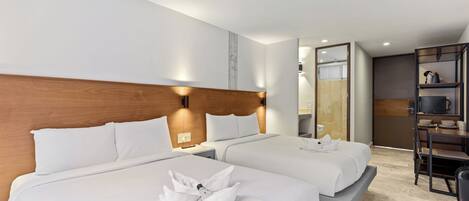 Una habitación de hotel con dos camas, un cabecero de madera, una mesita con lámpara y una pequeña cocina.