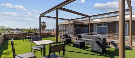 Une terrasse extérieure dotée d’une pelouse artificielle verte, d’un aménagement avec des sièges et d’une structure de toit en métal.