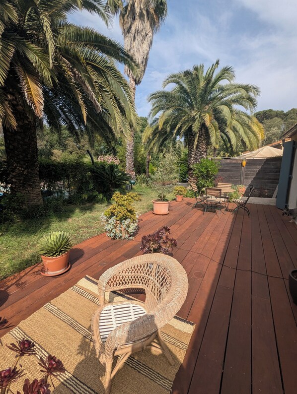 Une terrasse en bois avec un fauteuil en osier, entourée de plantes en pot et de palmiers.