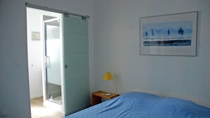 A bedroom with a bed, a nightstand with a lamp, a door leading to another room, and a framed picture on the wall. - Charming House : Swimming pool, Tennis court, Greenery, Near the sea (Bormes-les-Mimosas)