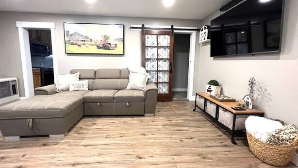 A living room with a sectional sofa, a flat-screen TV mounted on the wall, a wooden floor, and a sliding barn door. - Salmon Goldbug Cottage, hot tub sleeps 8 (Salmon)