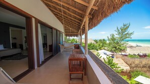 A balcony with a view of the beach, wooden furniture, and a thatched roof.