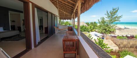 Un balcón con vista a la playa, muebles de madera y un techo de paja.