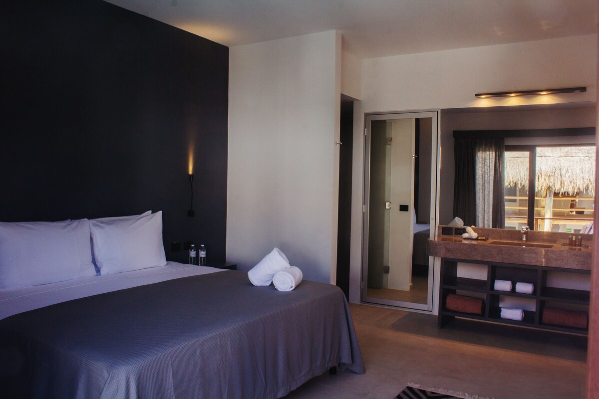 A modern hotel room with a large bed, a bathroom with a vanity, and a sliding door leading to a balcony.