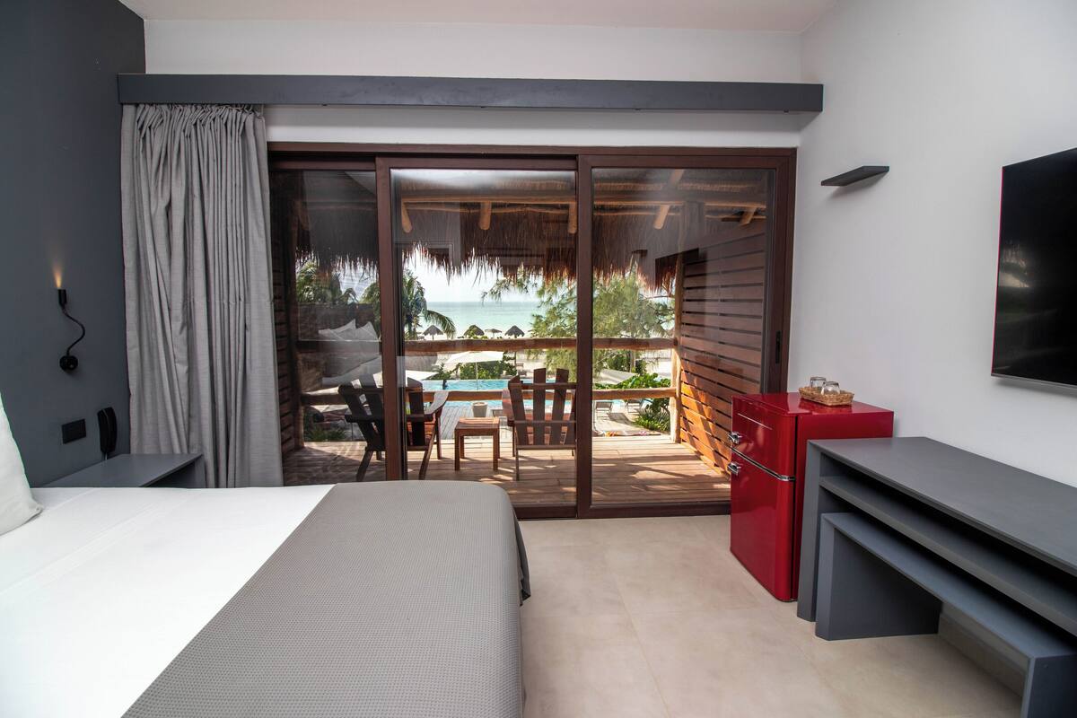 Quarto com cama, televisão, escrivaninha e varanda com piscina e cadeiras.