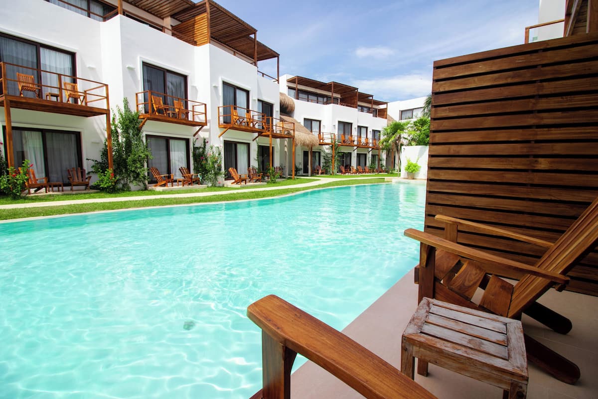 Um hotel com piscina, cadeiras de madeira e fachada de prédio branca.