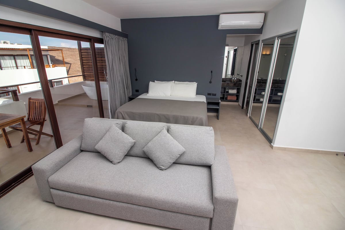 Quarto moderno com uma cama grande, um sofá cinzento e uma varanda com vista.