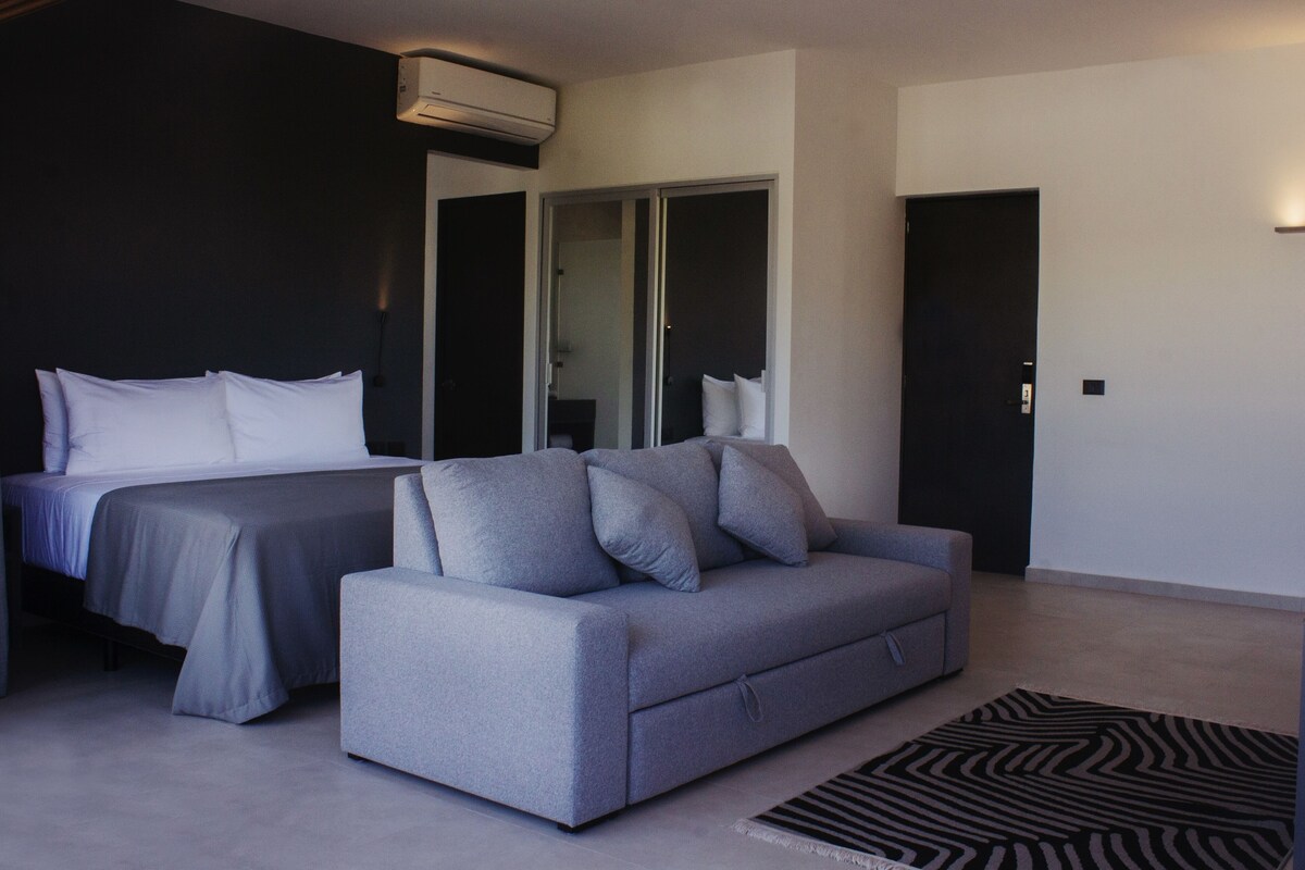 A modern hotel room with a bed, a sofa, a wardrobe, and a door.