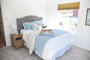 A bedroom with a bed, bedside table, lamp, and window with blinds.