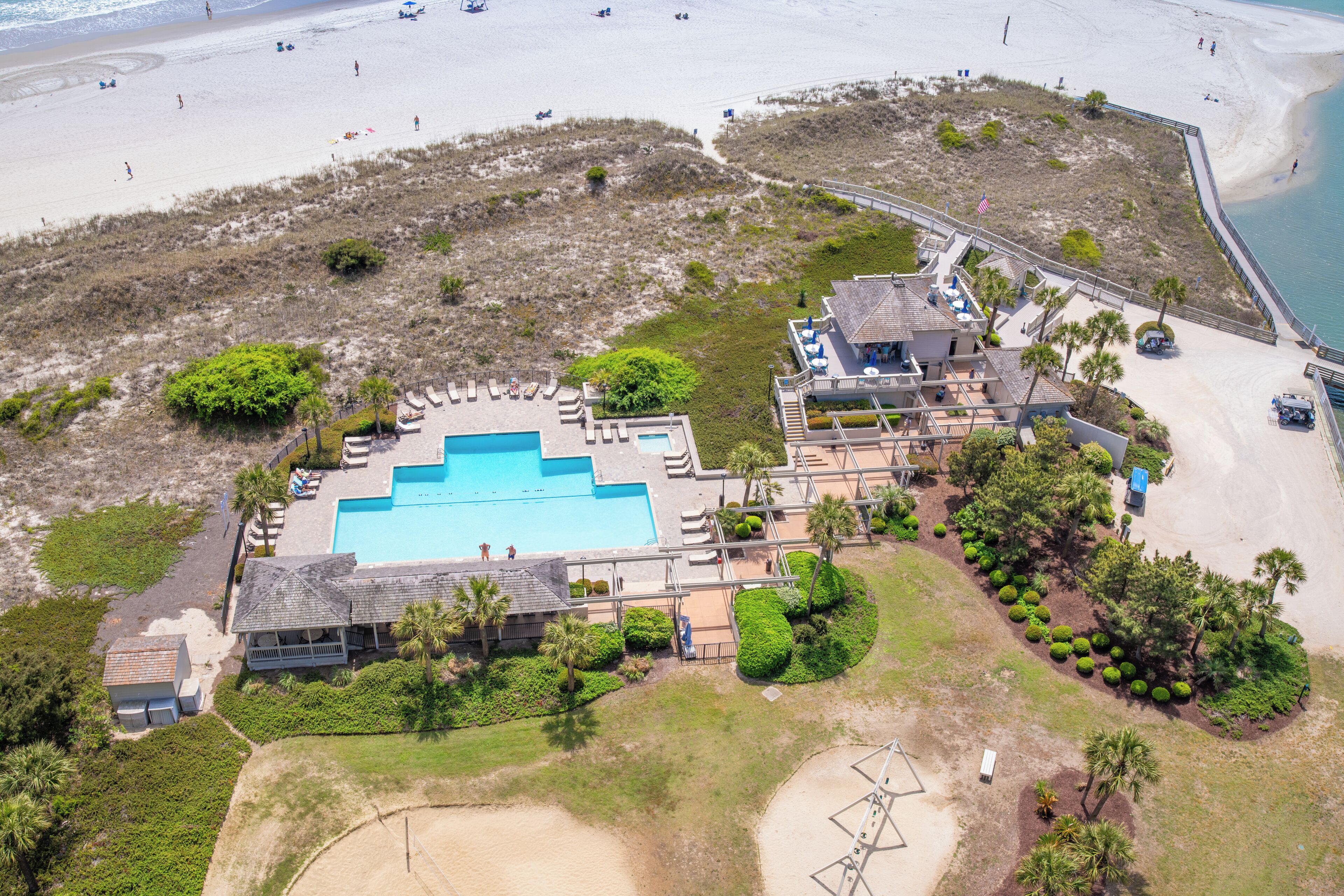 An aerial view of a resort with a swimming pool, beach access, and a large building with multiple rooms.