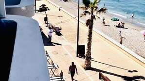 A beach with a palm tree, a bench, and a person walking. - BALERMA BEACH (El Ejido)