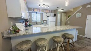 A kitchen with a marble countertop, white cabinets, and a bar area with stools. - Spacious 2BR/2.5BA Two-Story Beach House, Pet Friendly, FREE Golf Cart Included (Panama City Beach)