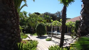 A wooden deck with a swing set, surrounded by tropical plants and a stone wall. - Apartment in a quiet, private estate with swimming pool, tennis court and petanque area (Bormes-les-Mimosas)