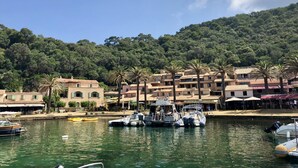 A marina with boats docked, a waterfront building with balconies, and a hillside with dense trees. - Apartment in a quiet, private estate with swimming pool, tennis court and petanque area (Bormes-les-Mimosas)