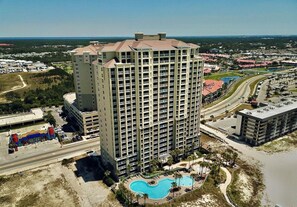 A high-rise hotel with a swimming pool and a view of the surrounding area. - Grand Panama 902 - Gulf Front, Beach Chairs, Pets OK + Amenities (Panama City Beach)