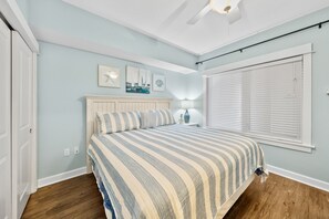Ein Schlafzimmer mit einem Bett, einem Deckenventilator, einem Fenster mit Jalousien und Kunstwerken an der Wand.