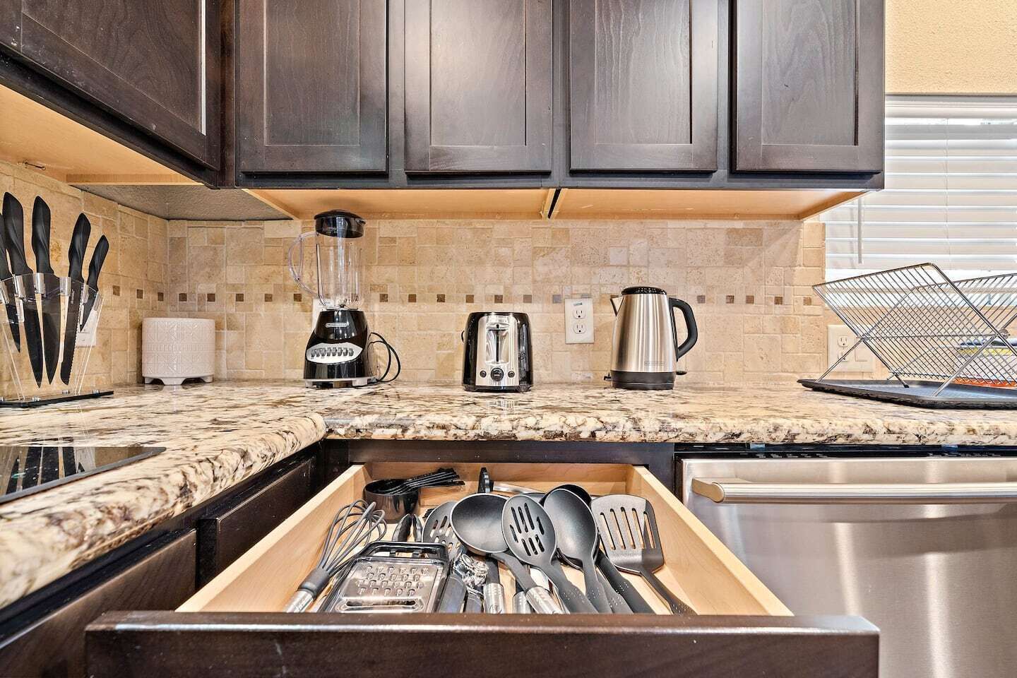 A kitchen with dark wooden cabinets, a granite countertop, a blender, a toaster, and a kettle.