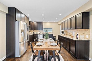 Eine moderne Küche mit dunklen Holzschränken, Edelstahlgeräten und einem Holzesstisch, gedeckt für sechs Personen.