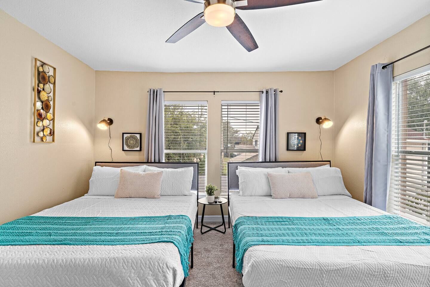 Une chambre d’hôtel avec deux lits, un ventilateur de plafond, une petite table et une vue par la fenêtre.