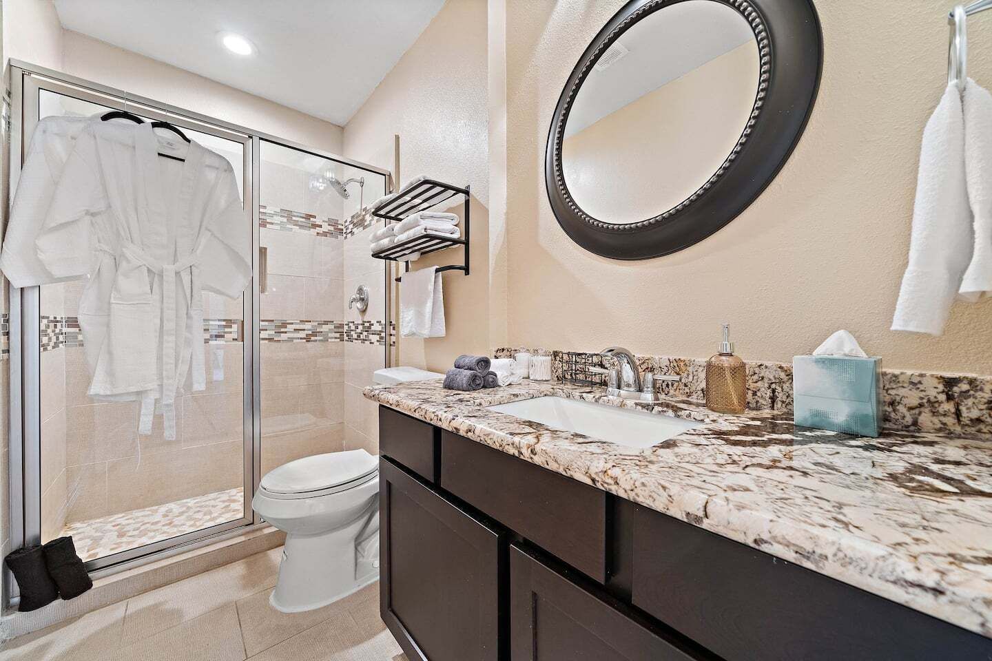 A bathroom with a glass shower enclosure, a toilet, a sink with a marble countertop, a mirror, and a towel rack.
