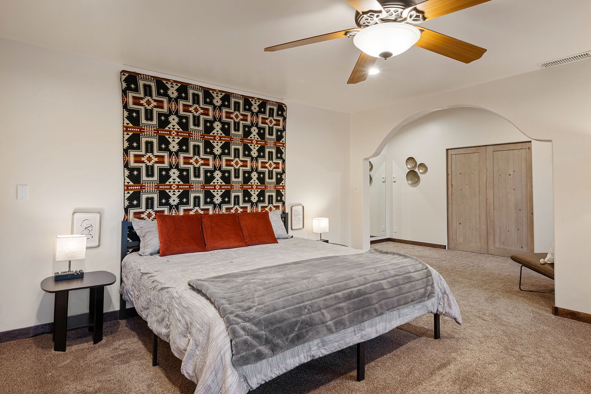 A bedroom with a large bed, a ceiling fan, a patterned wall, and a wooden wardrobe.