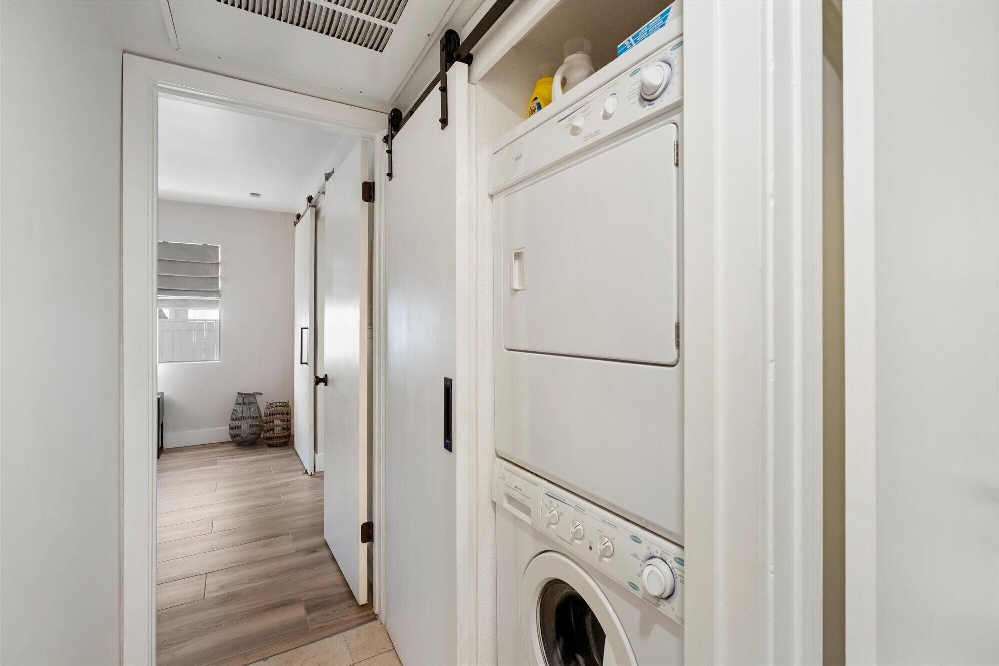 Une buanderie équipée d’un lave-linge et d’un sèche-linge, avec un plancher en bois et une porte donnant sur une autre pièce.