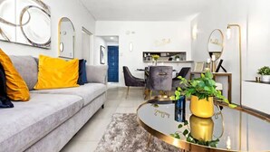 A modern living room with a grey sofa, yellow cushions, a round coffee table with a plant, and a dining area in the background.