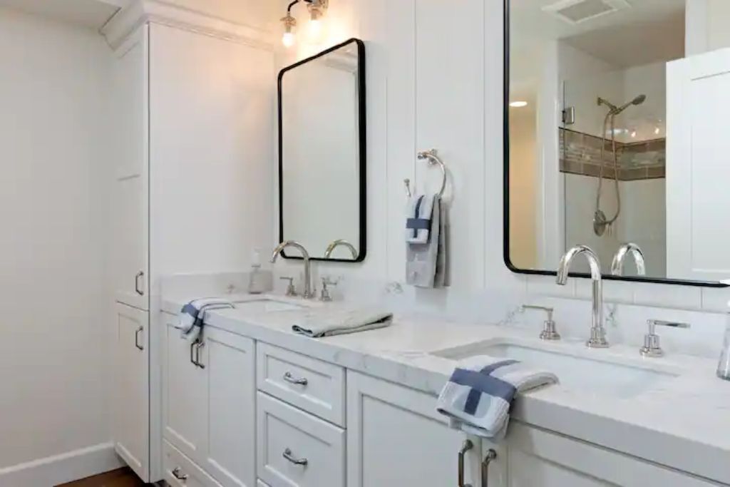 A modern bathroom with white cabinetry, a large mirror, and a shower area.