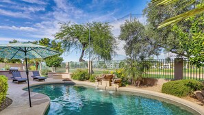 A swimming pool with lounge chairs and an umbrella, surrounded by trees and a fence. - Golfer Oasis w/ Pool & Putting Green in Goodyear! (Goodyear)
