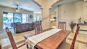 A spacious dining area with a wooden table and chairs, a view of the kitchen, and a ceiling fan. - Golfer Oasis w/ Pool & Putting Green in Goodyear! (Goodyear)