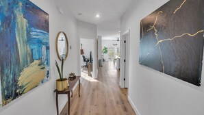 A hallway with wooden flooring, a large abstract painting on the left, a mirror on a small table, and a large painting on the right. - NEW Luxury pool home w/hot tub, KING bed, close to beach, firepit (St. Petersburg)