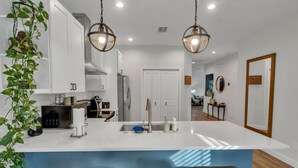A modern kitchen with white cabinetry, a central island with bar stools, and pendant lighting. - NEW Luxury pool home w/hot tub, KING bed, close to beach, firepit (St. Petersburg)