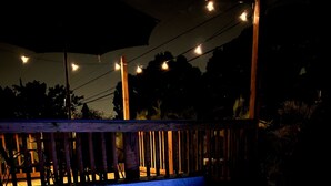 A hot tub with a wooden deck and string lights, surrounded by trees. - NEW Luxury pool home w/hot tub, KING bed, close to beach, firepit (St. Petersburg)