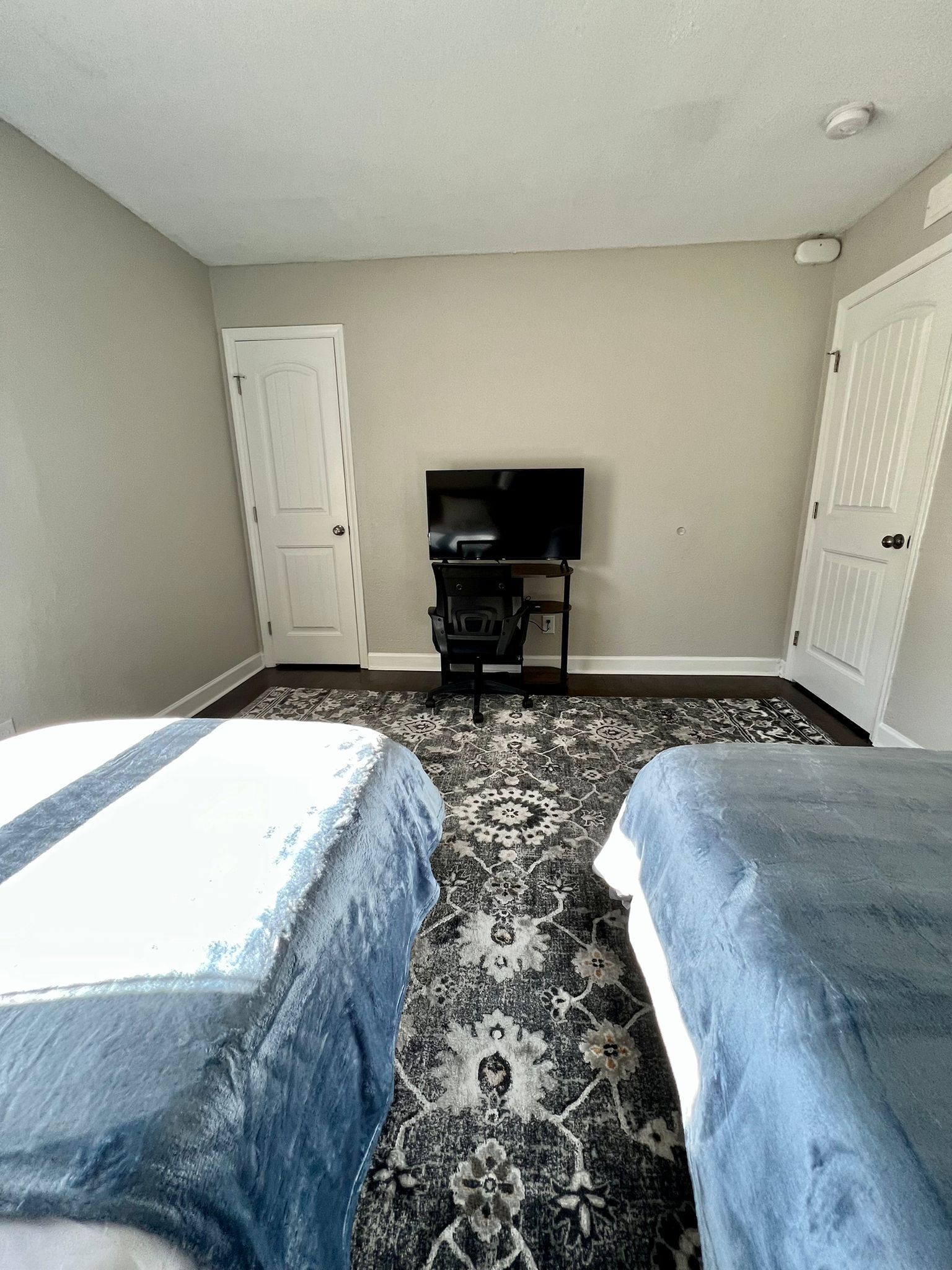 Habitación de hotel con dos camas, televisión, escritorio y alfombra estampada.