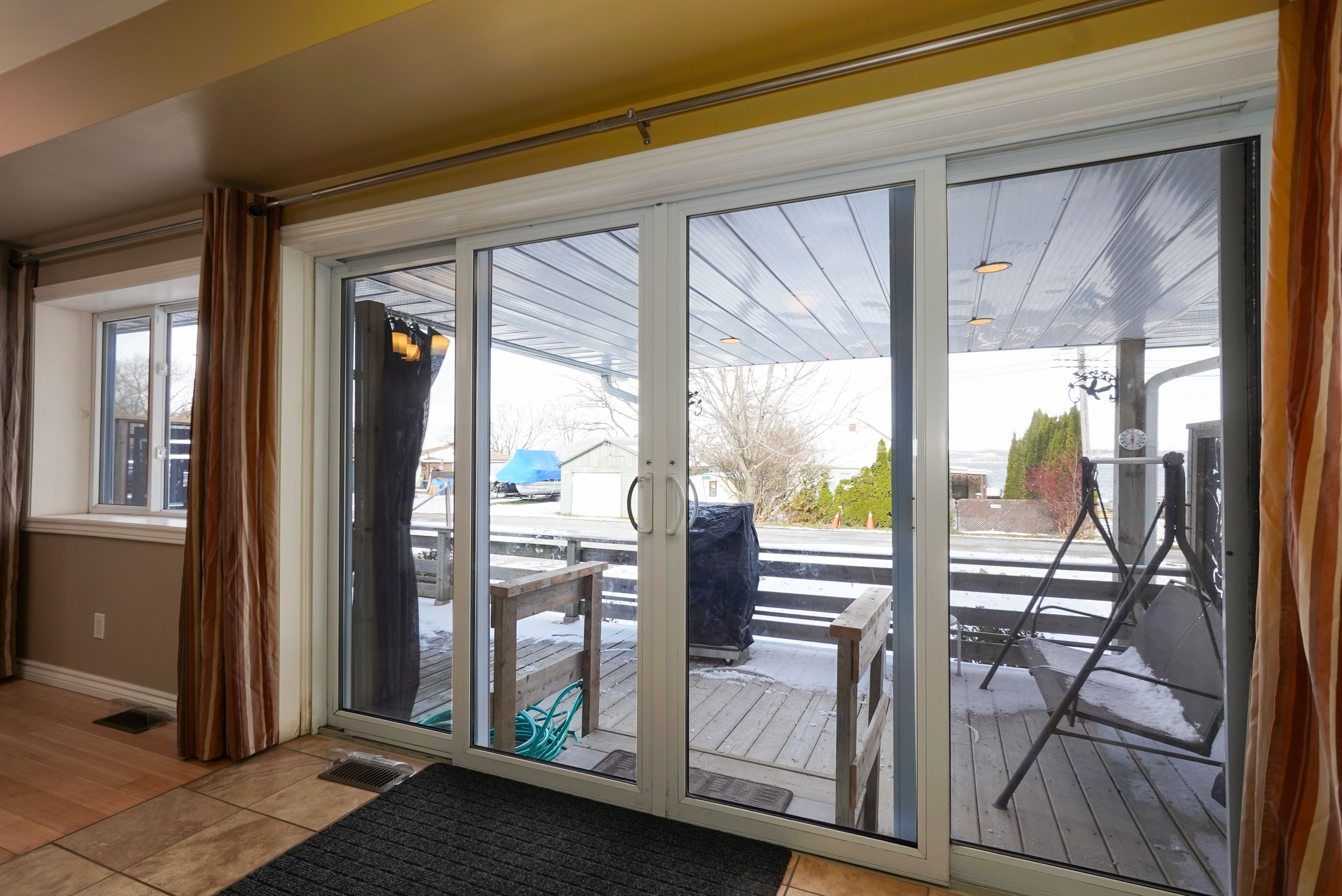 A room with a sliding glass door leading to a covered outdoor area with a wooden deck, a covered seating area, and a covered patio with a swing set.