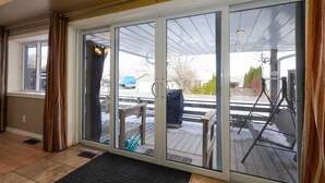 Une pièce dotée d’une porte-fenêtre coulissante donnant sur un espace extérieur abrité, comprenant une terrasse en bois, un coin salon couvert et un patio abrité avec une balançoire.