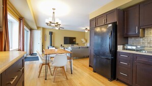 Une cuisine moderne avec des meubles de rangement en bois foncé, un réfrigérateur noir et un coin repas comprenant une table en bois et des chaises blanches.