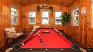 Une table de billard avec des queues de billard, une chaise en osier et une petite table sur laquelle est posée une plante.