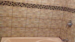 Un baño con pared de azulejos color beige, un borde de azulejos estampados y una bañera.