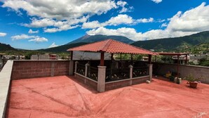 Una terraza en la azotea con techo de tejas rojas, una zona de estar cubierta y una vista de la montaña al fondo.