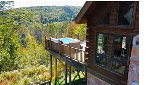 A wooden cabin with a hot tub on a deck, surrounded by forested hills. - Poconos True Log Cabin with Views, Hot Tub & Game Room (Mount Pocono)