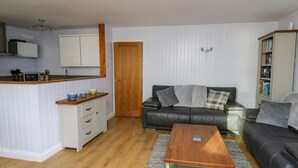 A compact living space with a kitchenette, a sofa, a coffee table, and a bookshelf. - 1 St. Marys Court (Tenby)