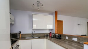 A modern kitchen with white cabinets, a stainless steel sink, a microwave, a toaster, and a wooden countertop. - 1 St. Marys Court (Tenby)