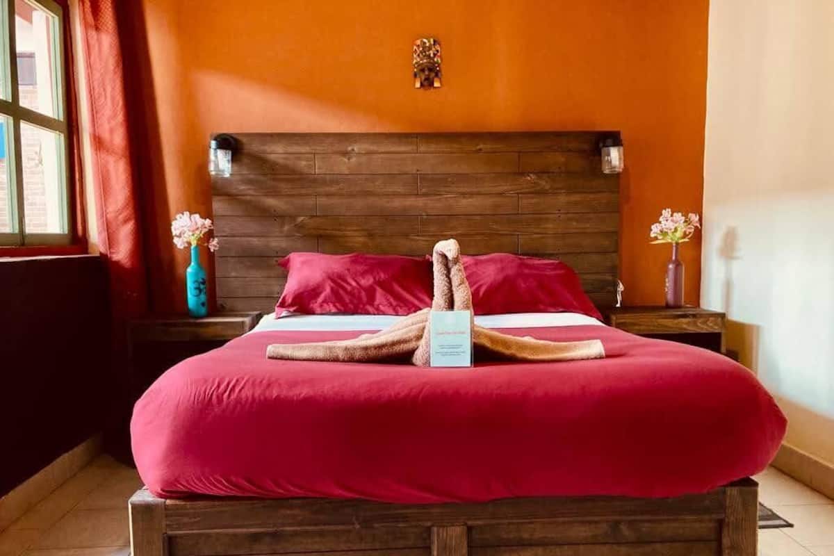 A bed with a wooden headboard, red bedding, and a decorative towel arrangement.