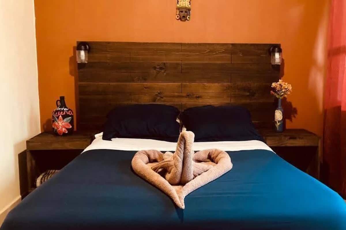 A neatly made bed with a towel in the center, a wooden headboard, two bedside tables with lamps, and a wall-mounted light fixture.